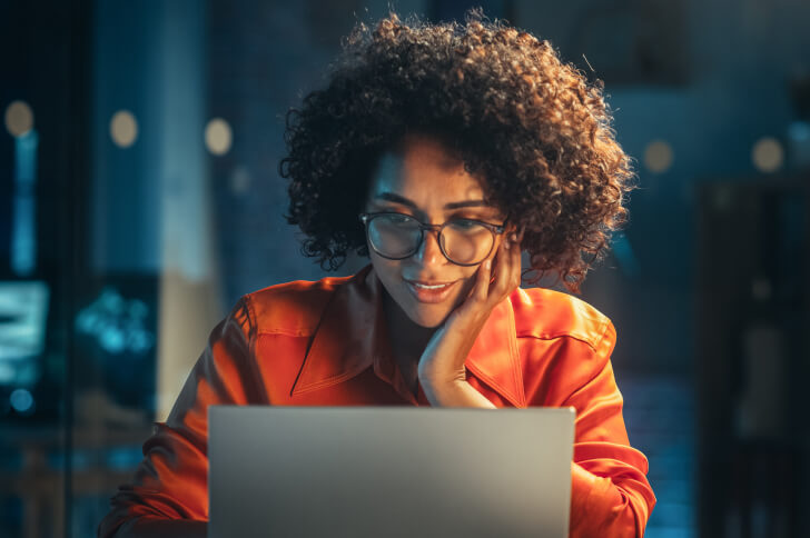Lady with hand on chin wearing glasses sat face on at a laptop