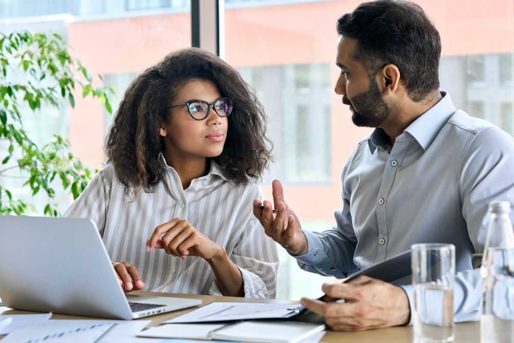 Lady Wiht A Laptop In Discussion With A Man Holding A Pen And Note Pad